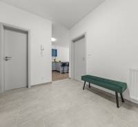 A hallway in a 2-room apartment with doors, a green bench, and a view into the kitchen.