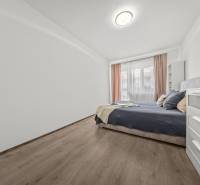 Bright bedroom with a double bed in a 2-room apartment, with wooden flooring and a white dresser.