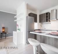A kitchen in a 2-room apartment with an island, open to the living room with a gray wall.