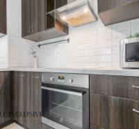 A kitchen in a 2-room apartment with appliances and dark wood, decorated with white tiles.