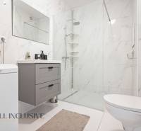 Bathroom in a 2-room apartment with white tiles, a shower, and white furniture.
