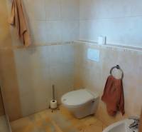 A bathroom in a family house with a shower, toilet, and bidet, with beige tiles.