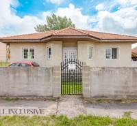 A family house in Selice with a red roof behind a concrete fence and a green yard.