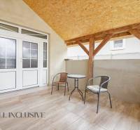 A covered terrace in a family house with rattan furniture and glass doors.