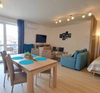 Studio apartment with a dining table, sofa, bed, and television, illuminated by lamps.
