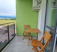 A balcony with a view and wooden furniture in a studio apartment. Green wall, air conditioning.