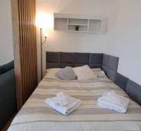 Studio apartment with a bed, wooden partition, floor lamp, and wall shelf with decorations.