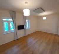 A room in a family house with a wooden floor, a television, and curtains on the windows.