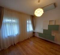 A room in a family house with laminate flooring, curtains, and wall shelves.
