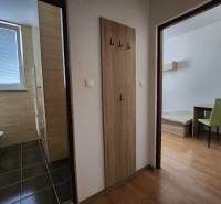 A hallway in a building with doors to a bathroom and a room with furniture.