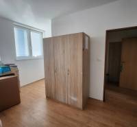 The interior of a building with wooden flooring, a wardrobe, cardboard boxes, and windows with blinds.