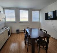 A kitchen with a wooden floor, table, chairs, kitchen unit, stove, and television on the wall.