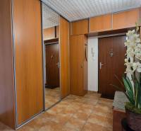 A hallway in a 2-room apartment with wooden cabinets, a mirror, and decorative flowers.