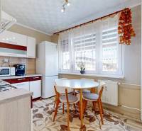 A kitchen in a 2-room apartment with a round table, a white refrigerator, and kitchen cabinets.