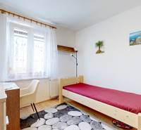 A bedroom in a two-room apartment with a bed, a table, a chair, and decorations on the wall.
