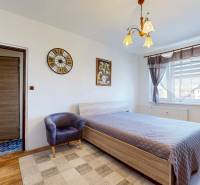 Bedroom in a two-room apartment with a bed, armchair, decorative clock, and painting.