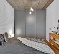A bedroom in a family house with a bed, wooden furniture, and a brick wall cladding.