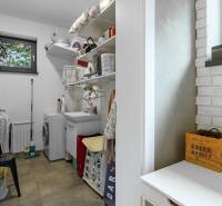 A laundry room in a family house with a sink, washing machine, and shelving storage.