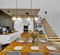 Dining room with kitchen, wooden table, flowers, and staircase in a family house.