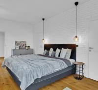 A bedroom in a family house with a wooden floor, a gray bed, and a white brick wall.