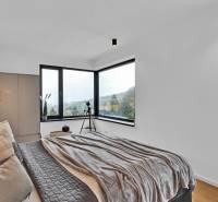 A room in a family house with windows, a bed, a chandelier, and a view of trees.