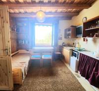 Wooden interior of a cabin with a kitchenette, bed, and dining table under the window.