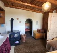 The interior of a cabin with a tiled stove, wooden furniture, and a simple bed.