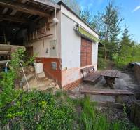 The cottage at Sychrov in Beckov; wooden benches and a table surrounded by greenery and trees.