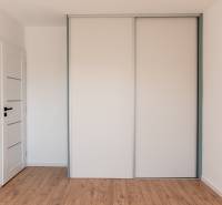 White built-in wardrobe with sliding doors in a 2-room apartment with wooden flooring.