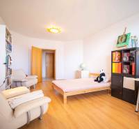 A bright room with wooden flooring in a 3-room apartment, containing a bed and a bookshelf.