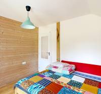 A room with wooden walls, a colorful bed, a wardrobe, and a light in a cabin.