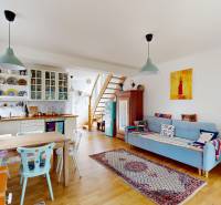 A bright room in a cottage with wooden furniture, a kitchen, and a piano playing corner.