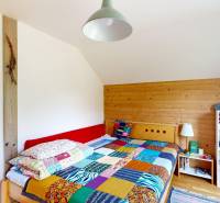 A bedroom in a cottage with a colorful blanket, wooden paneling, and a shelf.