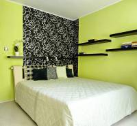 A bedroom with green walls, patterned wallpaper, a bed, and floating shelves. A 2-room apartment.