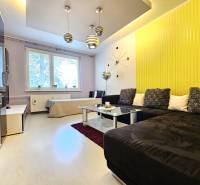 Living room in a two-room apartment with a yellow wall, brown sofa, and modern chandelier.