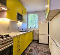 A kitchen in a 2-room apartment with yellow cabinets, a white refrigerator, and a stove.
