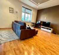 Living room in a two-room apartment with a sofa and a television, wooden floor and white walls.