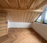Attic room in a cottage with a wooden ceiling, large window, and parquet floor.
