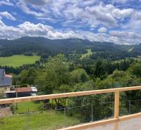 The view from the cottage in Korňa includes green meadows, hills, and a sky with clouds.