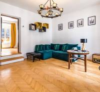 Living room in a 2-room apartment with wooden flooring, a blue sofa, and yellow curtains.