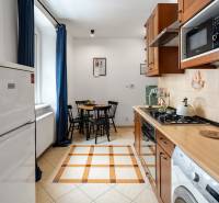 A kitchen with reddish-brown cabinets, a dining table, and a stove in a 2-room apartment.