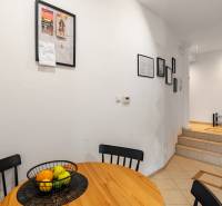 Dining area in a 2-room apartment with a wooden table, fruit bowl, and paintings.