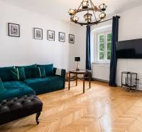 Living room in a two-room apartment with a sofa, wooden floor, and television.