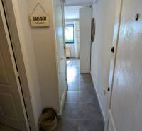 A narrow hallway in a studio apartment with baskets on the floor leads to a window.