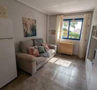 Studio apartment with a sofa, refrigerator, microwave, and a window with a view of trees.