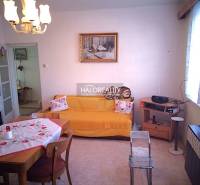 Living room of a family house with a dining table, sofa, and a radio on a shelf.