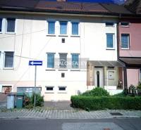 A family house in Nováky with a white facade, green shrubs, and a parking area in front of the house.