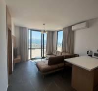 Living room in a holiday apartment with large windows, a sofa, and a kitchenette.