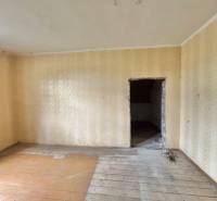A room in a family house with a wooden floor and beige wallpaper.