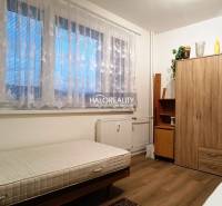 The room offers a simple bed and a wooden wardrobe in a 2-room apartment.